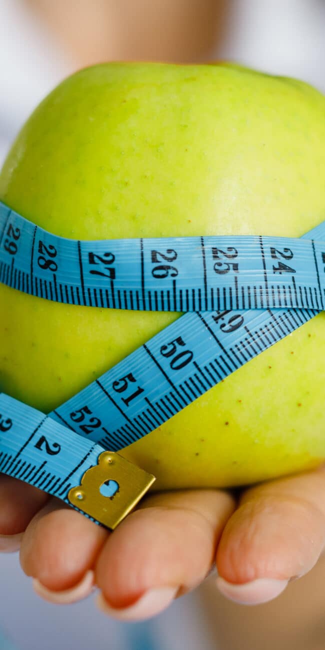 Apple with measuring tape on hand background. Weight loss, counting calories and healthy eating